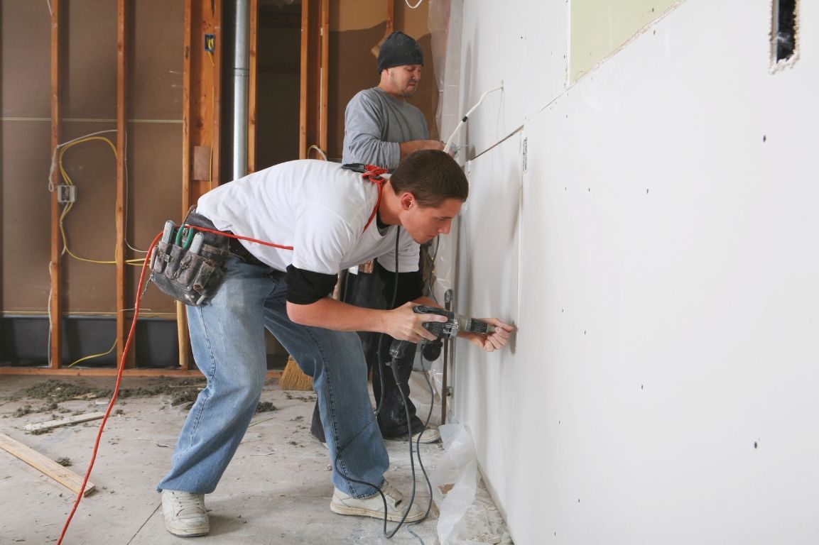 Two men are working on a wall with a drill.
