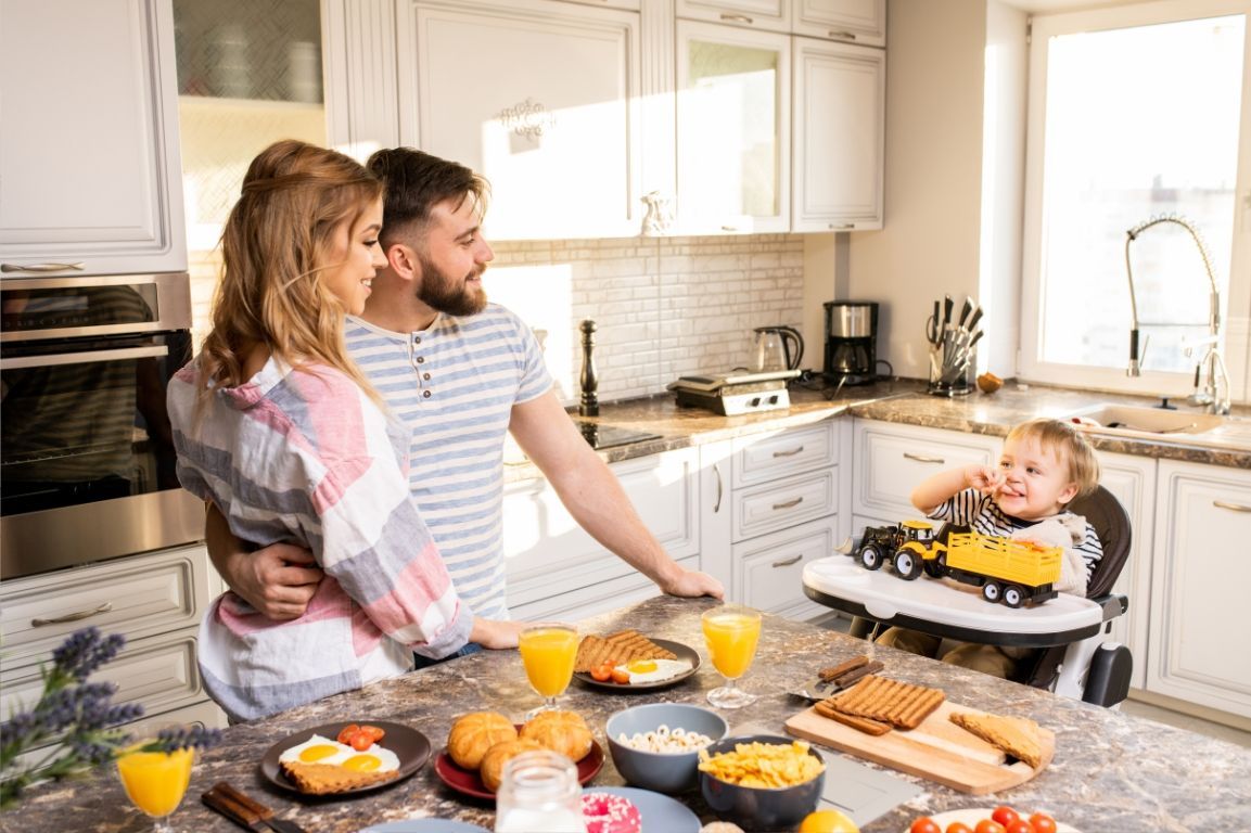 A family is having breakfast in the kitchen with a child in a high chair.