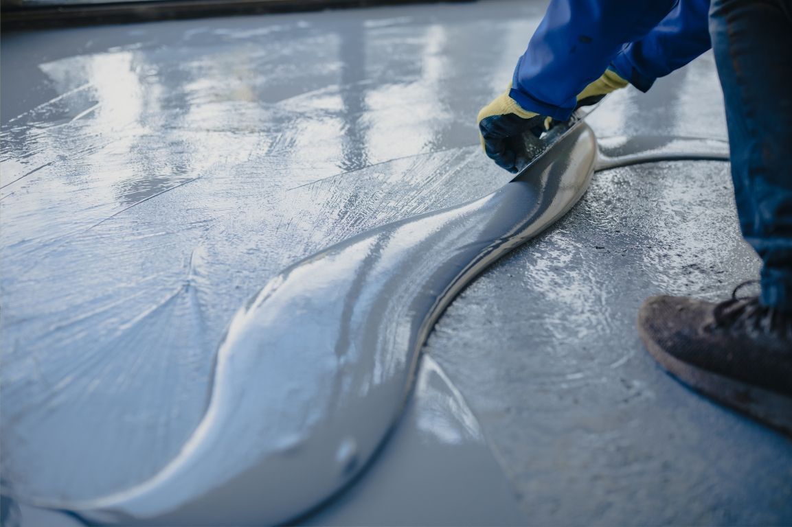 A person is spreading concrete on a floor with a spatula.