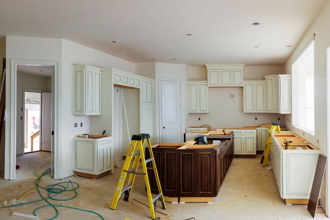 A kitchen is being remodeled in a house with a ladder in the middle of the room.