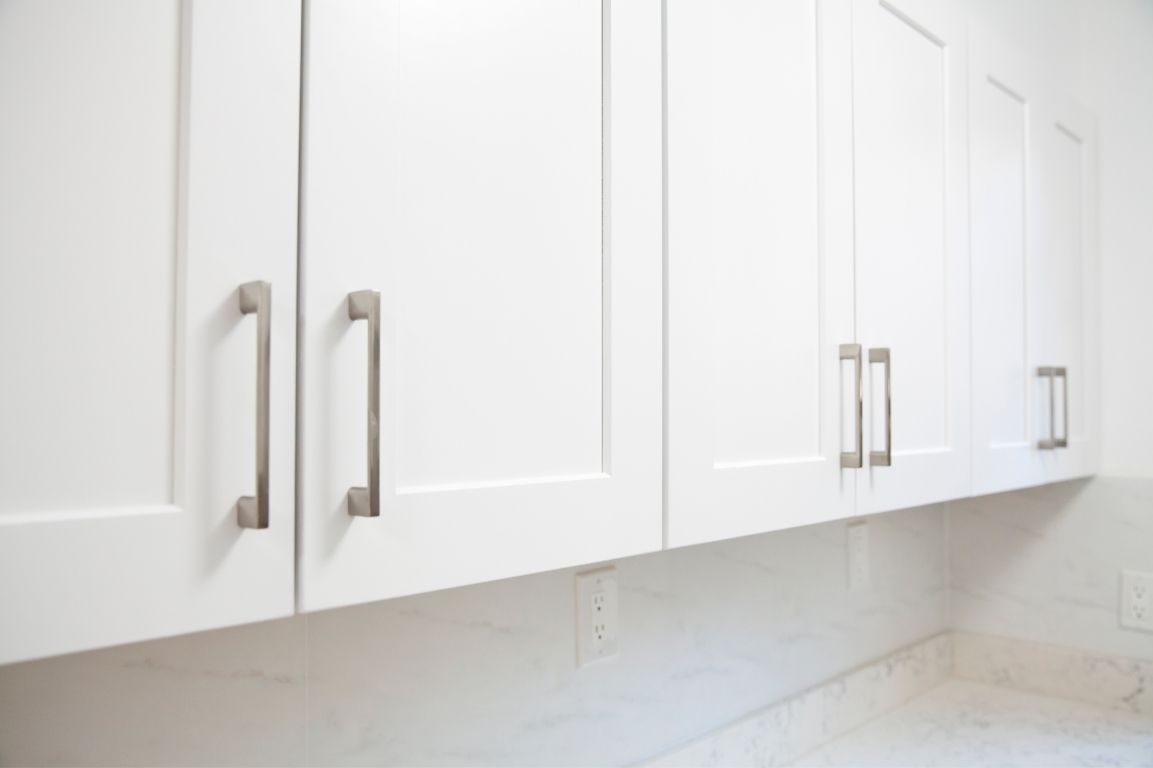 A kitchen with white cabinets and stainless steel handles.