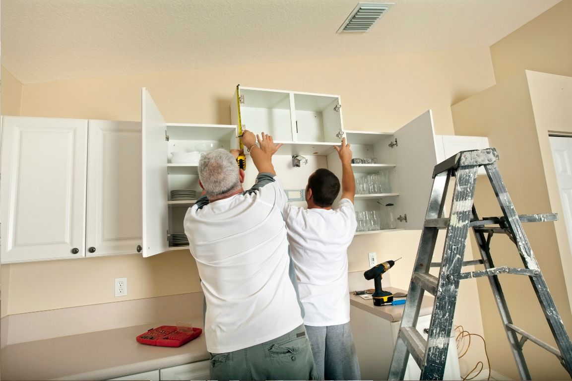 Two men are measuring a cabinet in a kitchen.