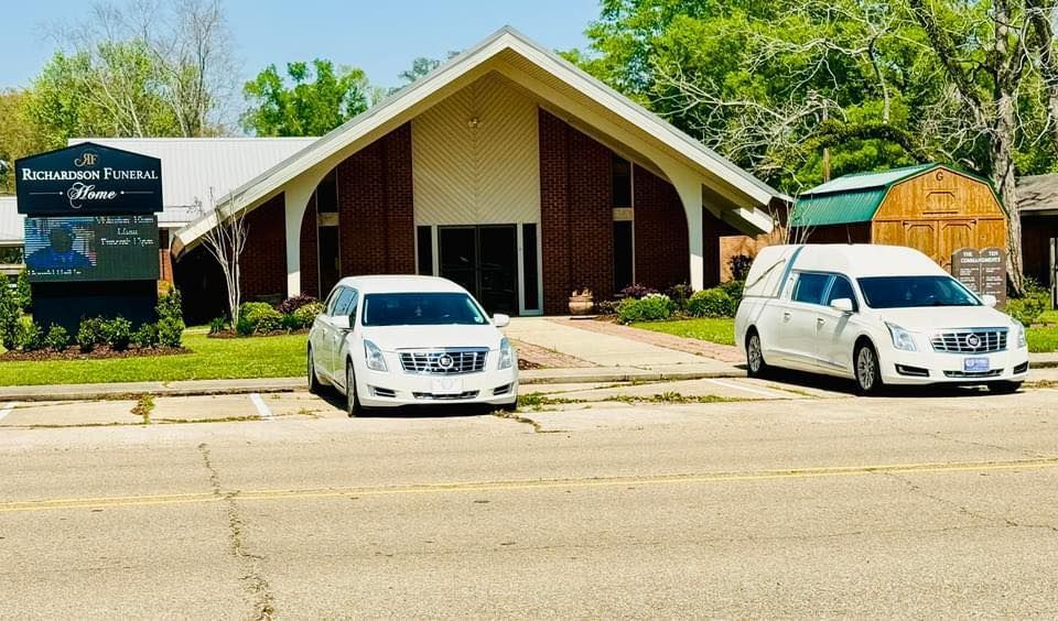 Brick building with peaked roof, two white vans parked in front, and a sign by the entrance