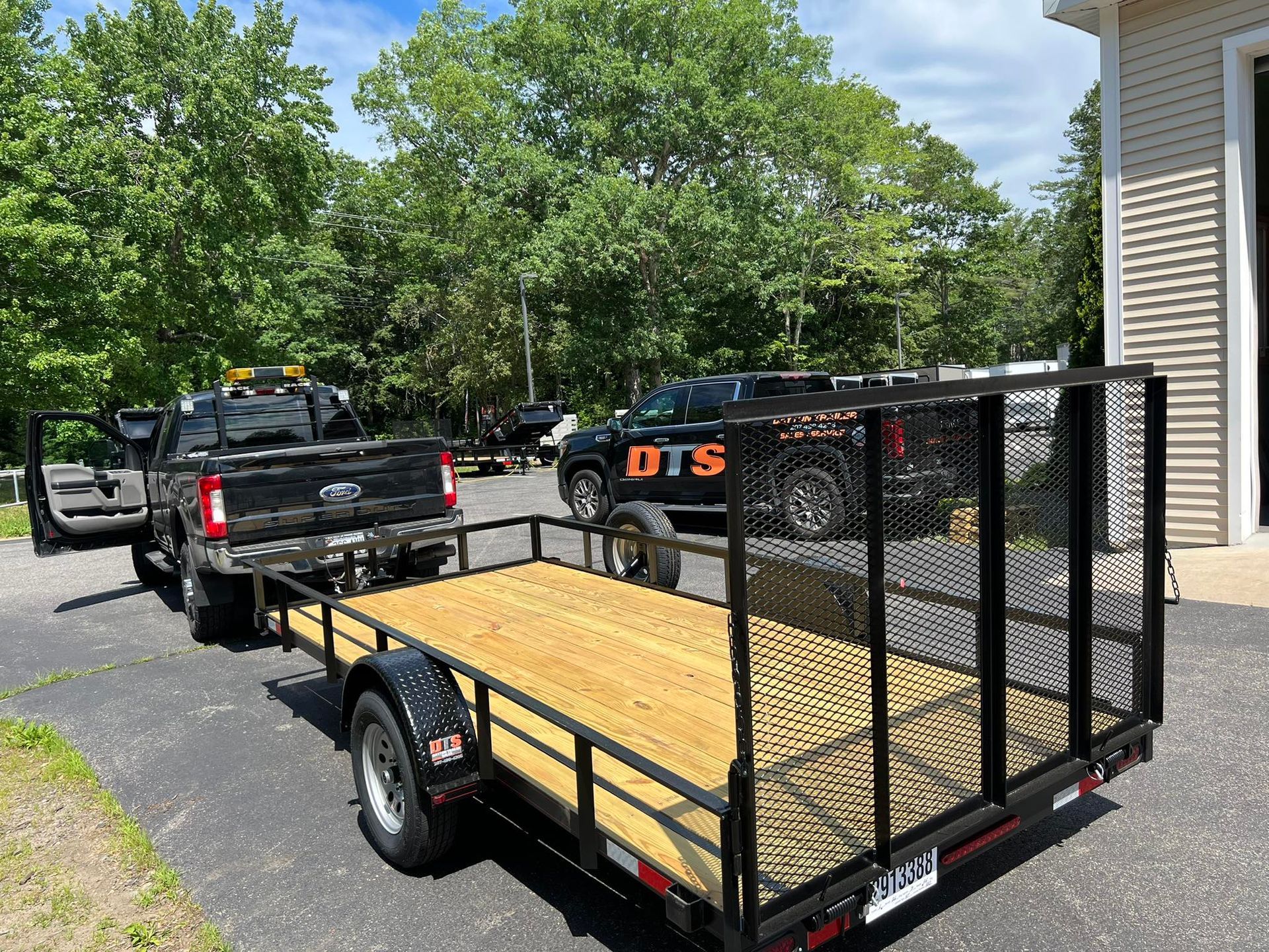 Black pickup truck towing a wood-deck utility trailer with mesh sides on a driveway