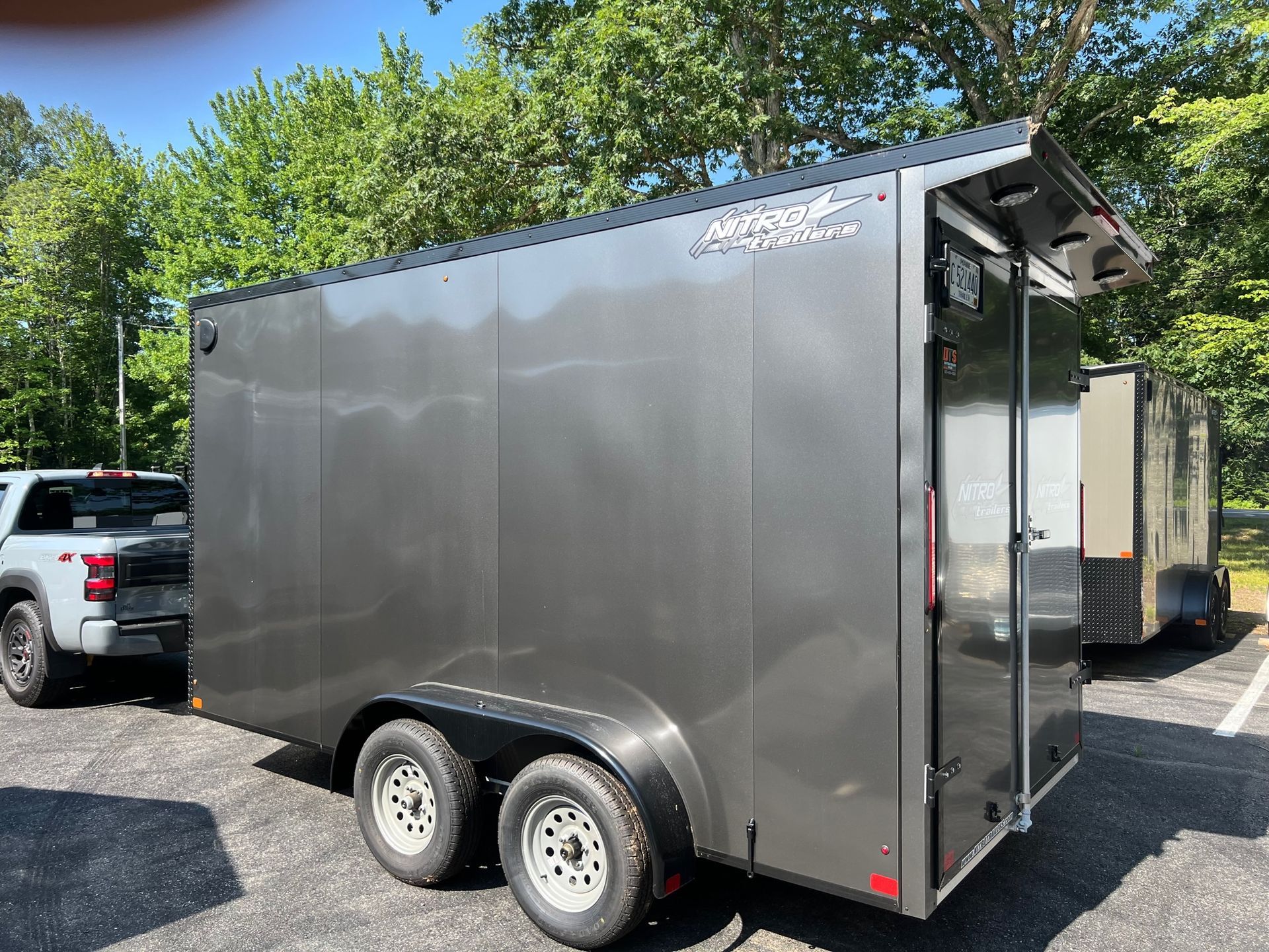 Silver enclosed cargo trailer parked outdoors on gravel beside a white pickup truck.