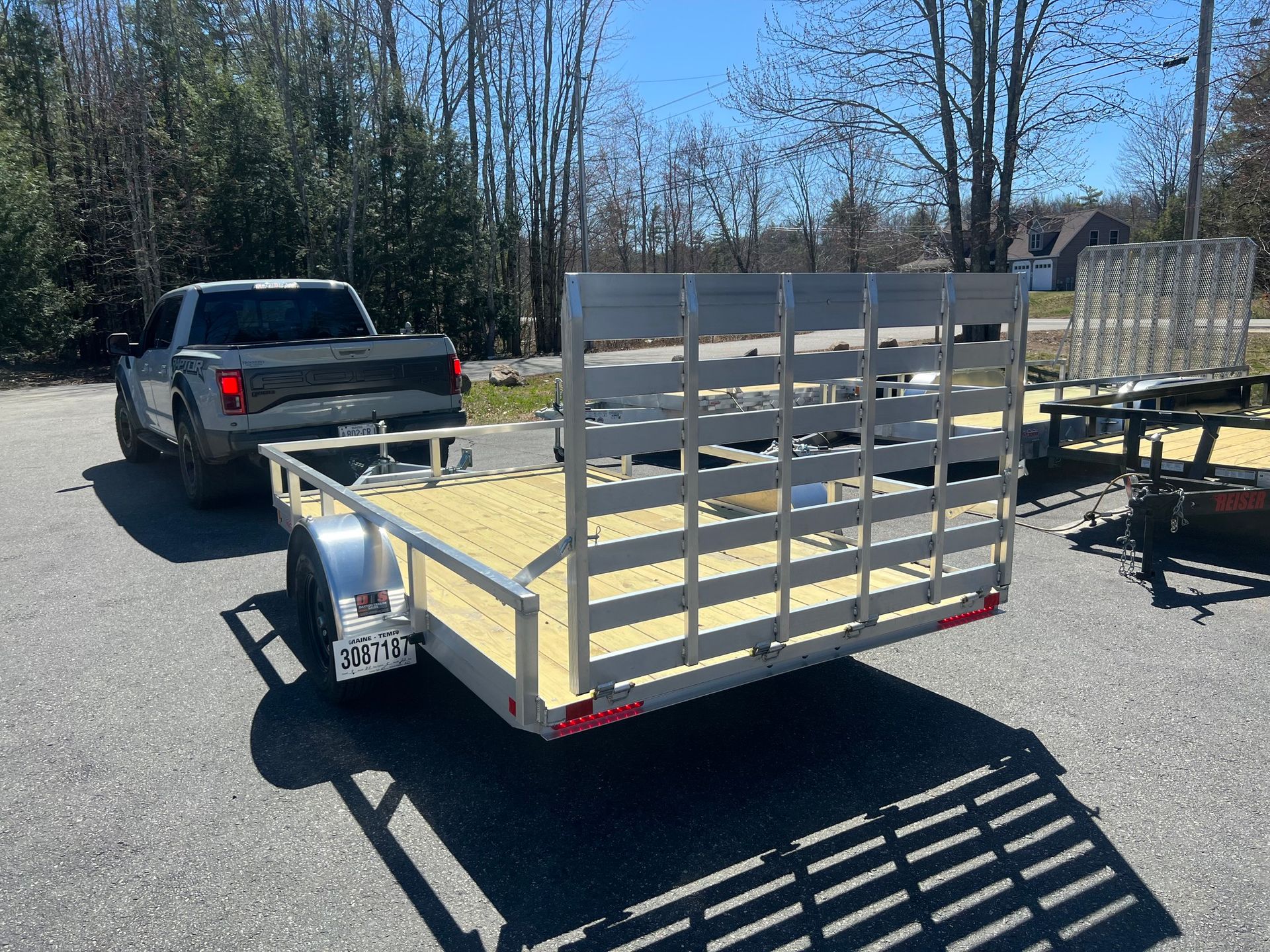 Gray pickup truck towing a small flatbed utility trailer with metal side rails in a sunny lot
