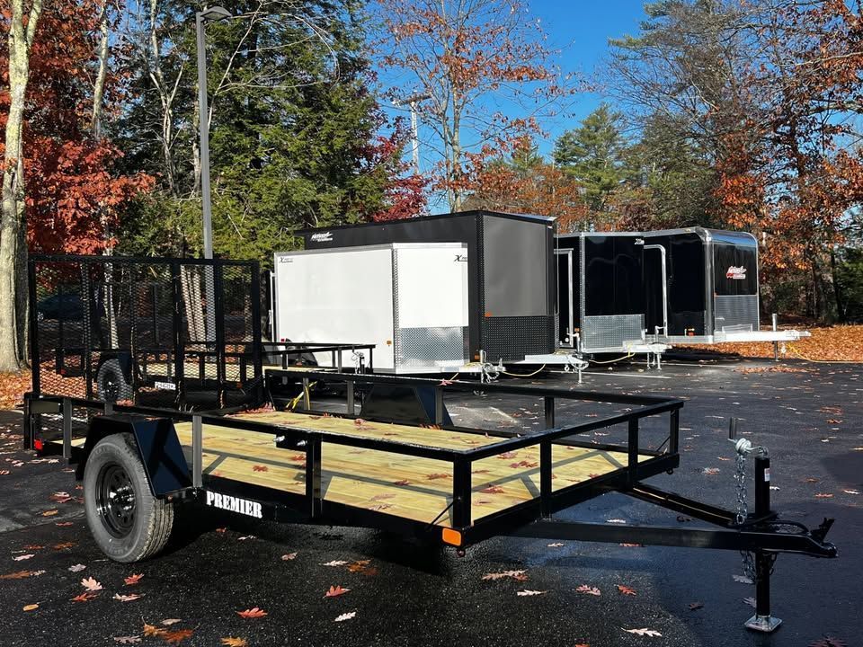 Black flatbed utility trailer parked outdoors with autumn trees and other trailers in the background