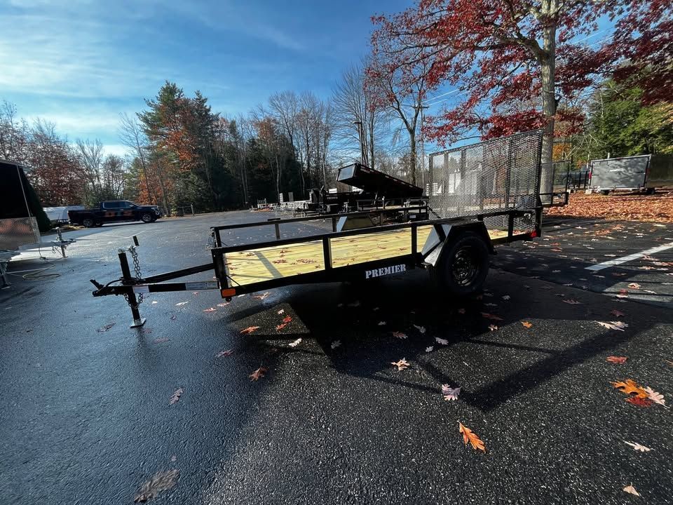 Black utility trailer on a wet road beside autumn trees and scattered fallen leaves.