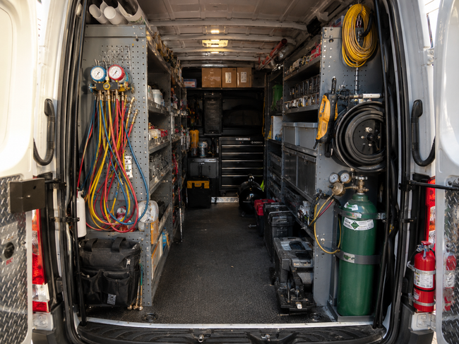 Interior of a utility van with tools, cables, gauges, and gas tanks along the walls.