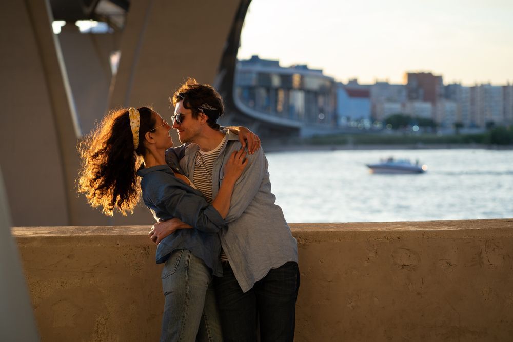 A man and a woman are kissing on a bridge over a body of water.