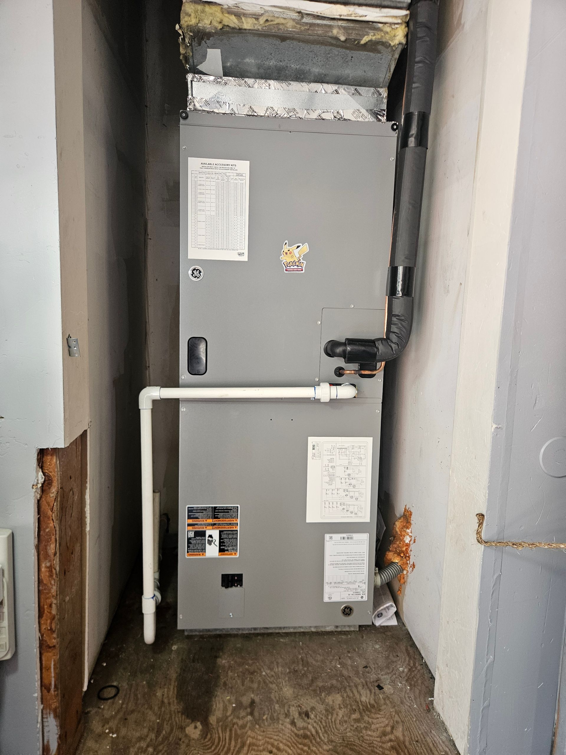 A gray HVAC unit in a narrow, concrete alcove. White pipe extends from the unit.