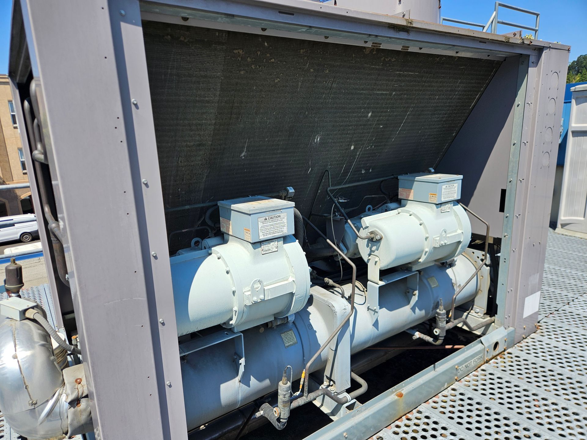 Two industrial air conditioning units on a rooftop, gray metal with cooling fins.