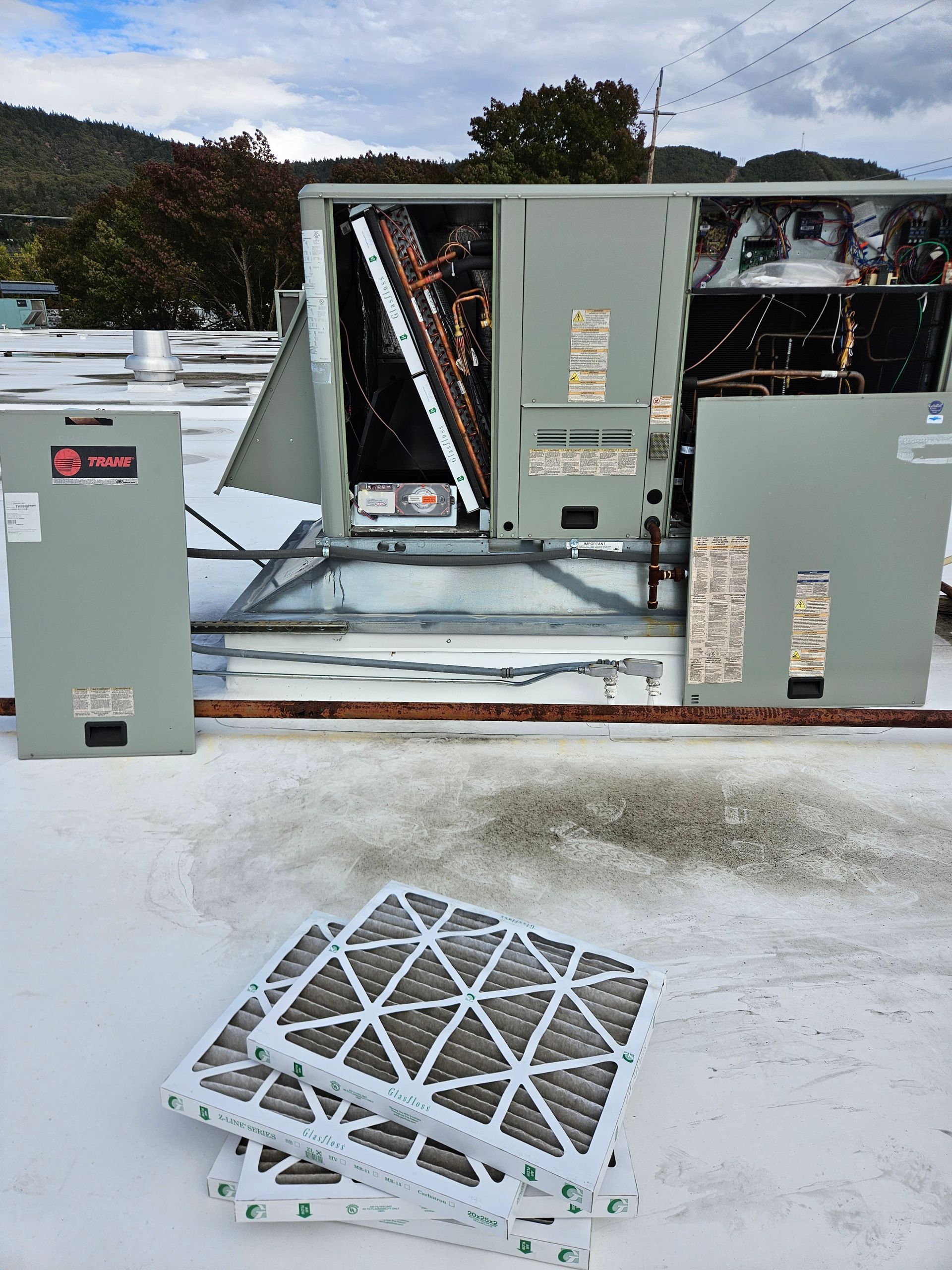 HVAC unit on a rooftop with open access panels and stacked air filters in the foreground.