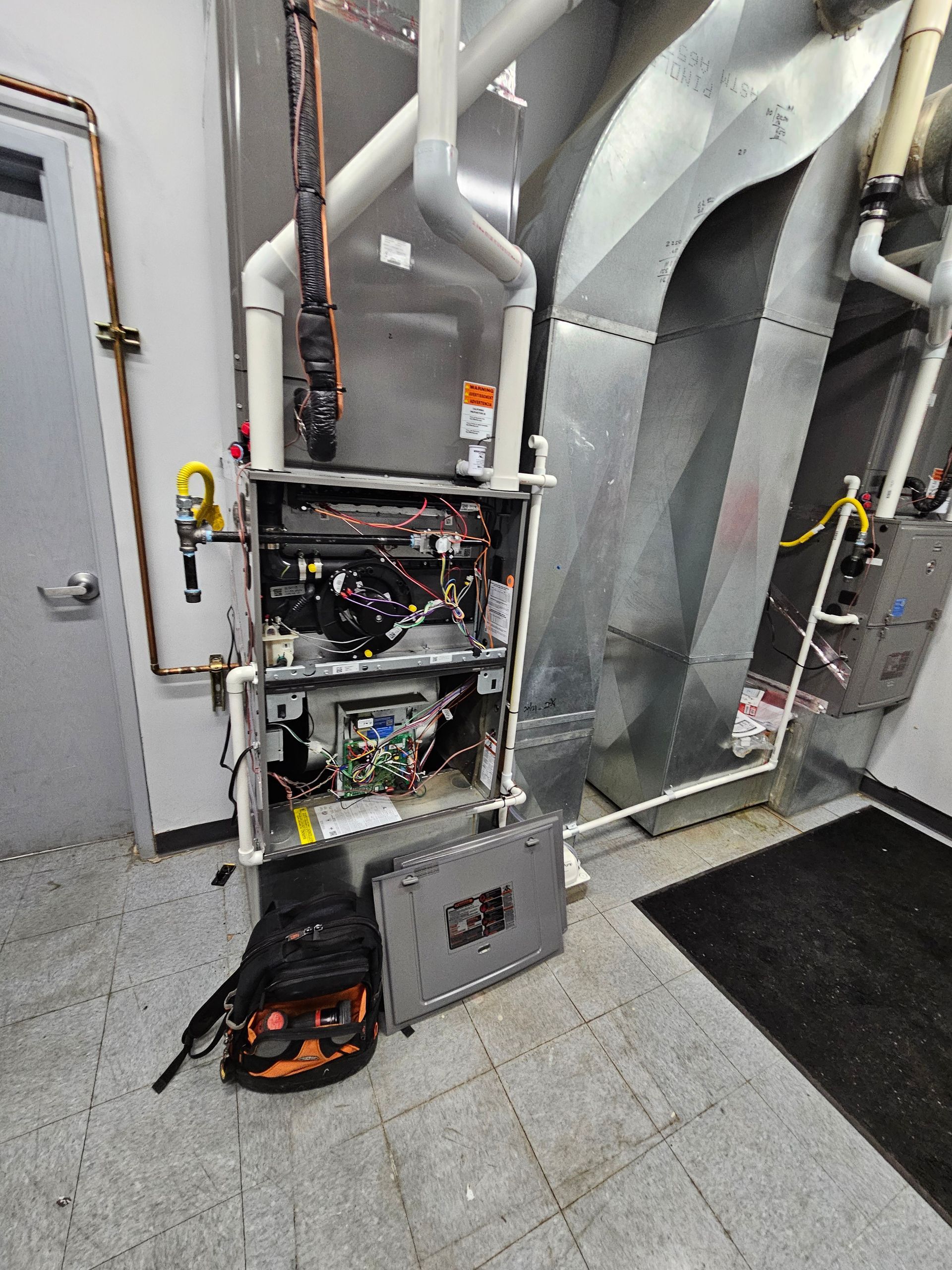 Furnace with open panels for maintenance, in a utility room. Ductwork, tools visible.