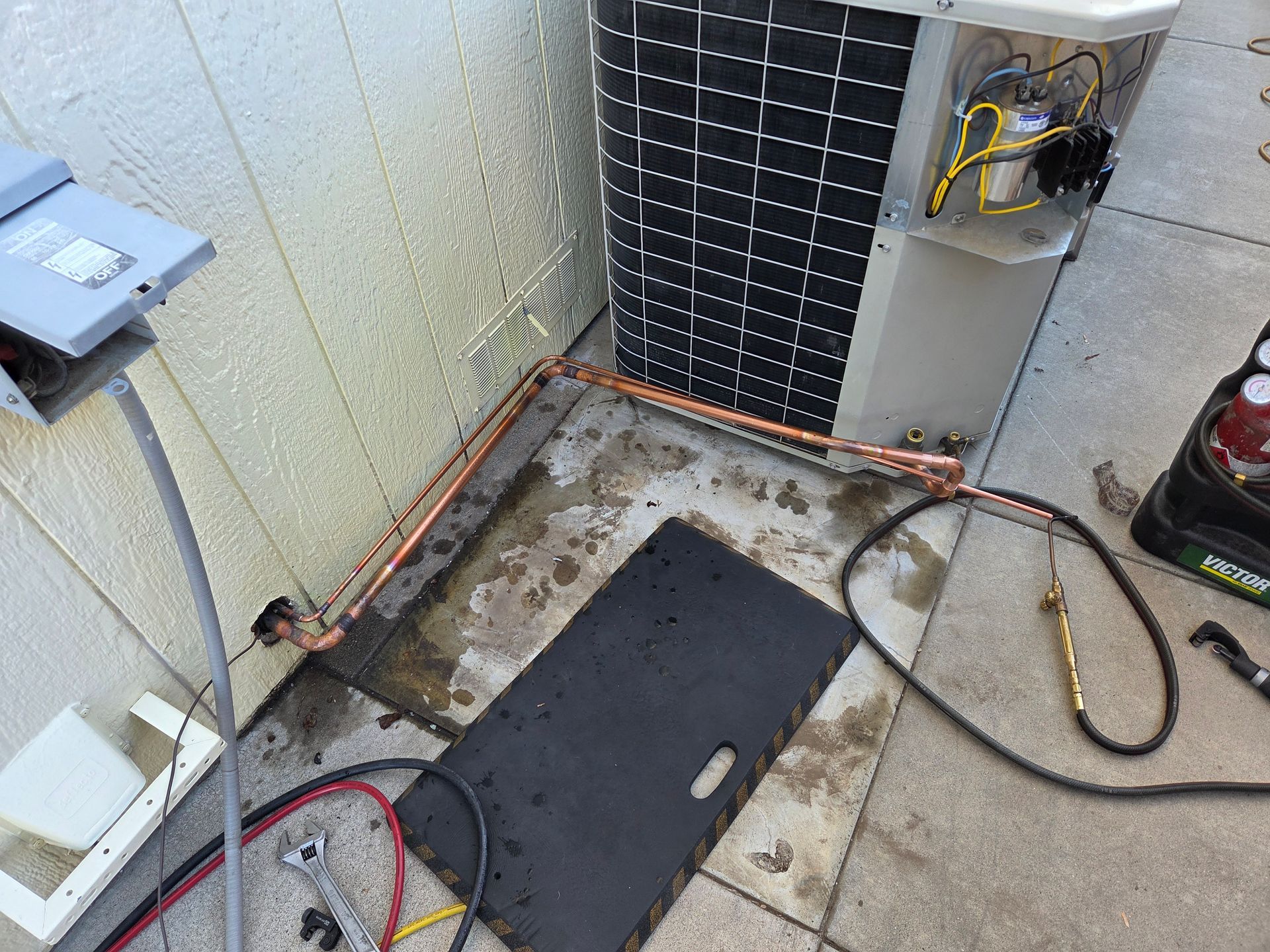 HVAC unit being serviced outdoors, copper piping visible. Tools and electrical components present.