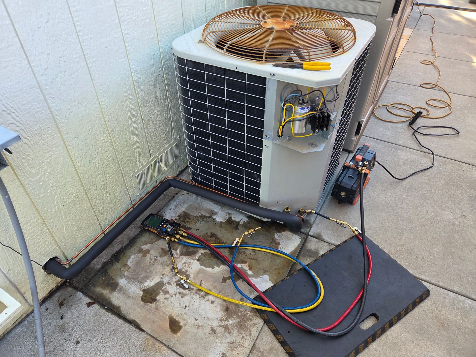Air conditioning unit being serviced outdoors, with hoses connected to a vacuum pump.