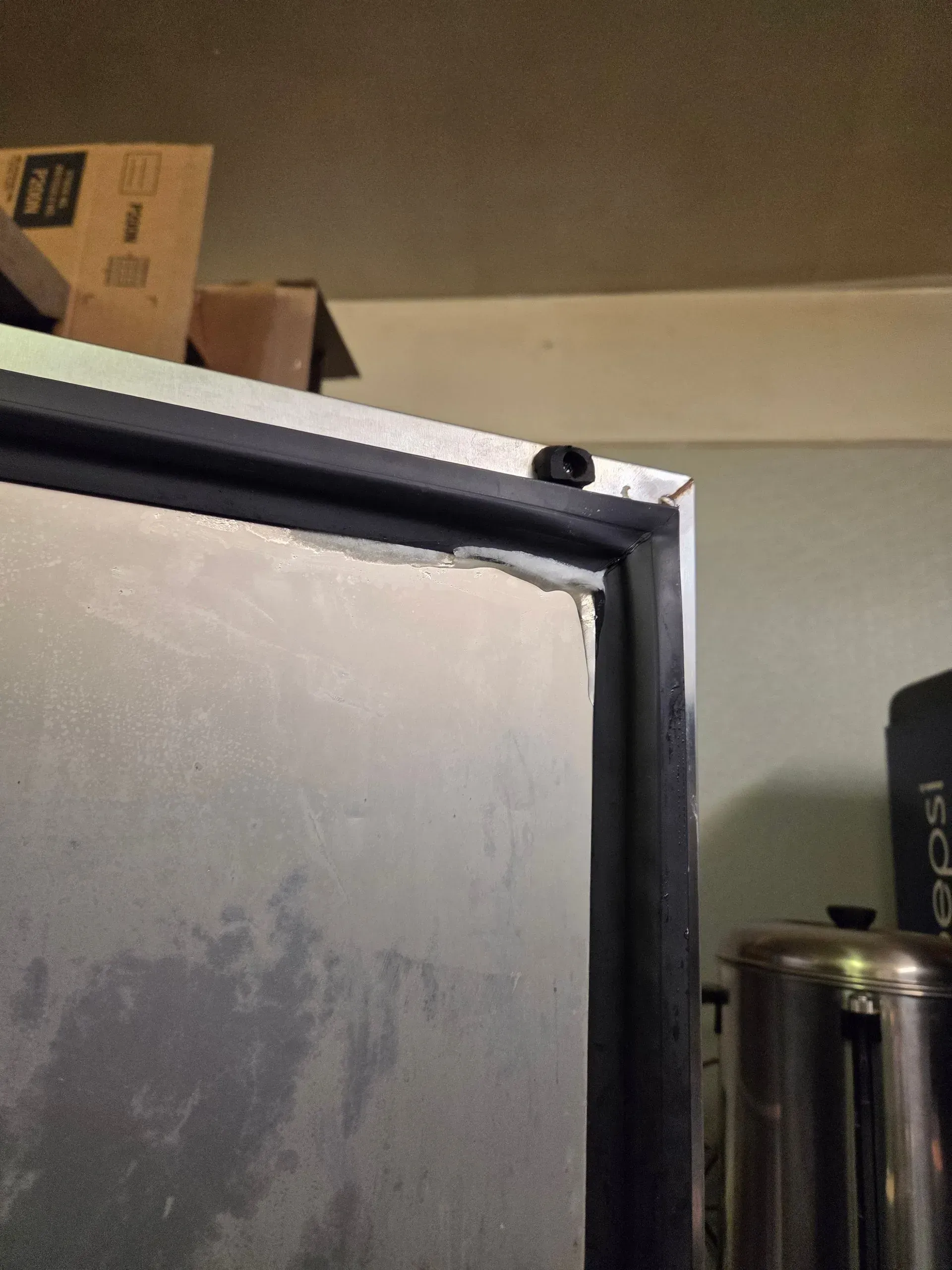 Corner of a metal appliance with a black rubber seal; a small black object sits atop.