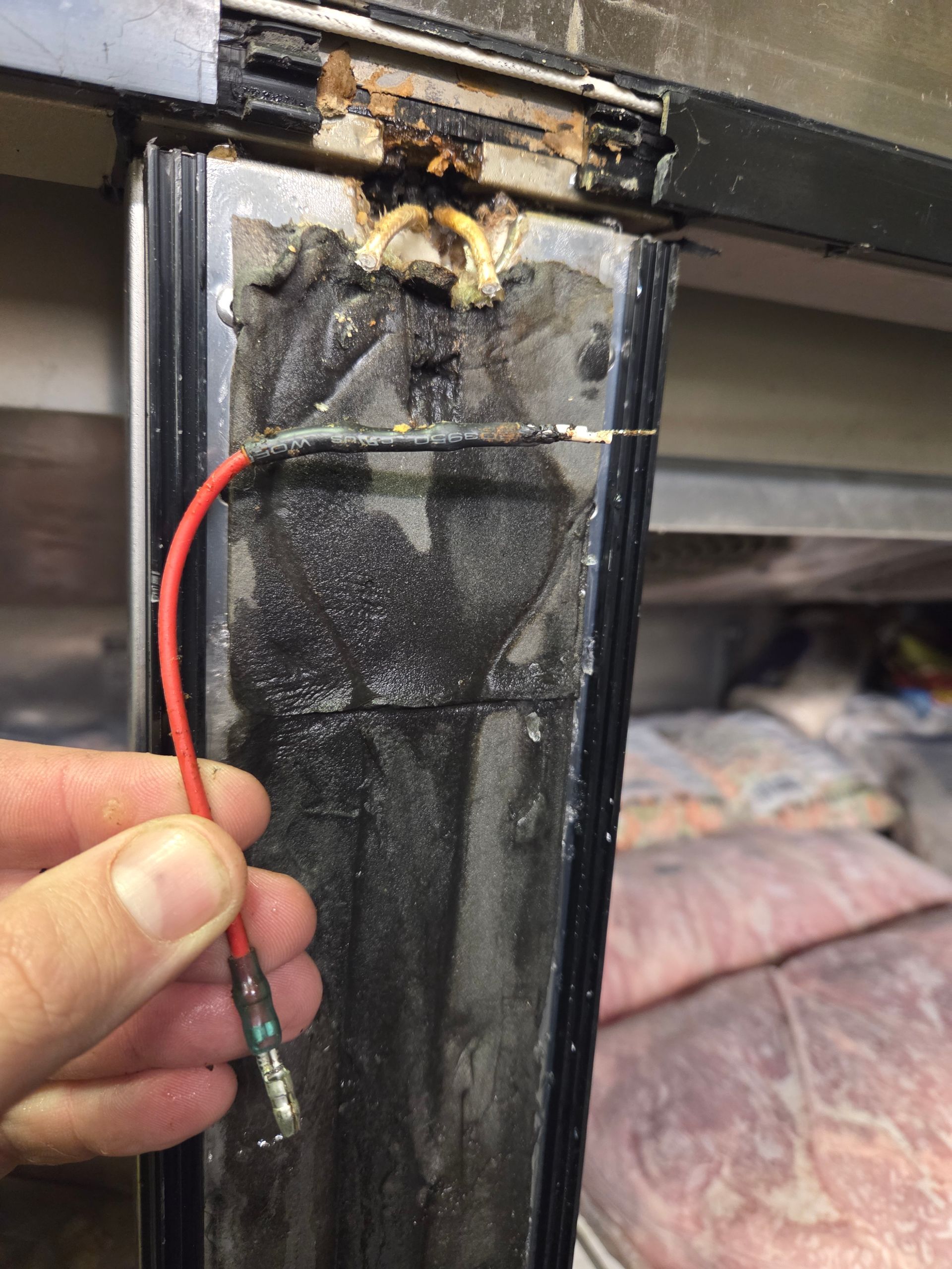 A hand holding a red wire connected to a damaged glass door frame with electrical issues.