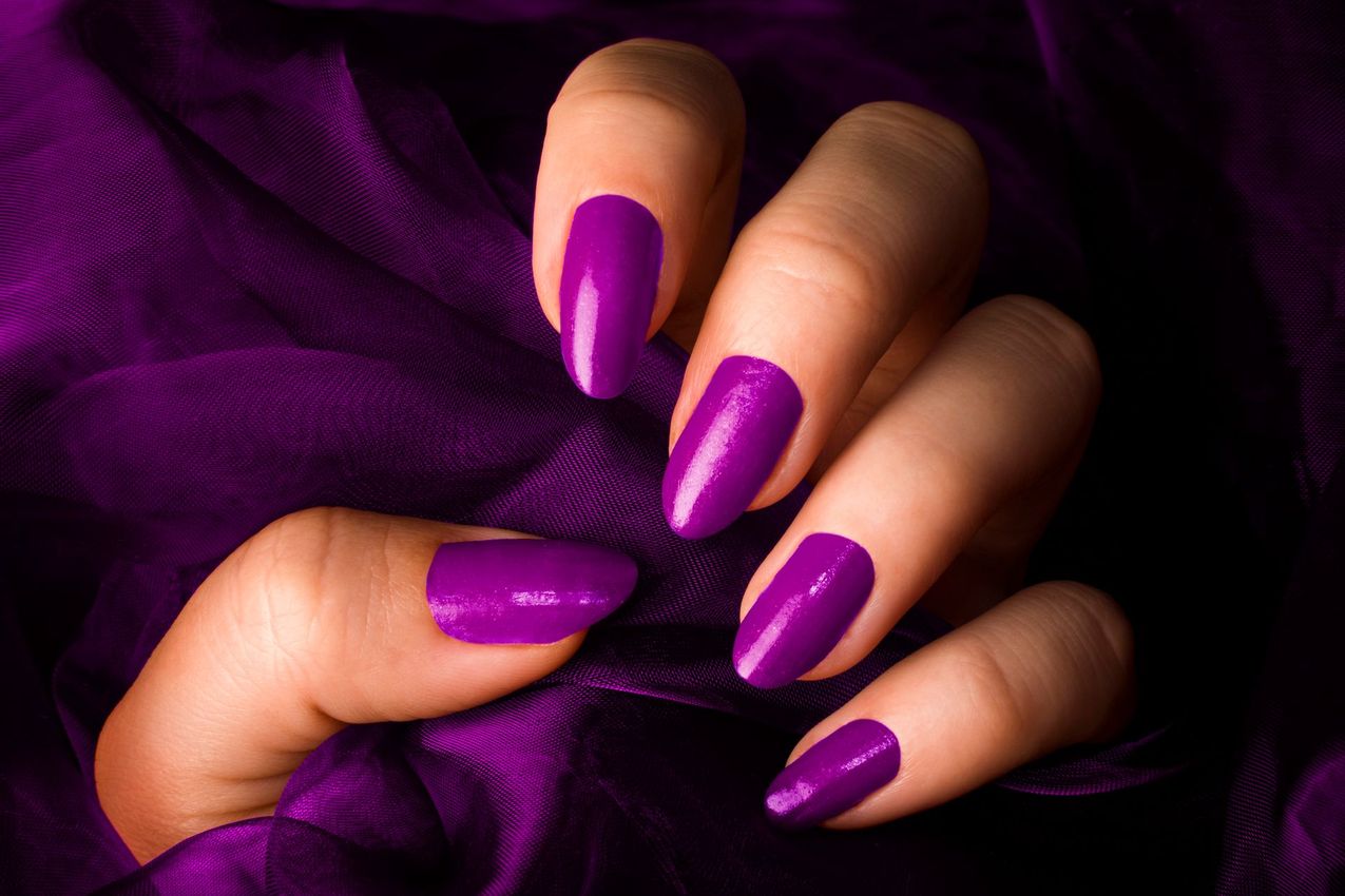 Mano con unghie lucide e laccate di viola, appoggiata su un tessuto viola scuro.
