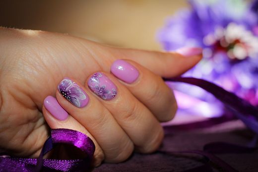 Mano con smalto viola lucido e glitterato accanto a un nastro viola su una superficie viola tenue