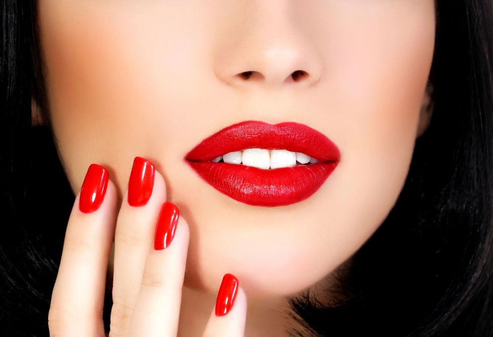 Primo piano di labbra rosse lucide e unghie rosse abbinate che sfiorano il mento di una donna.