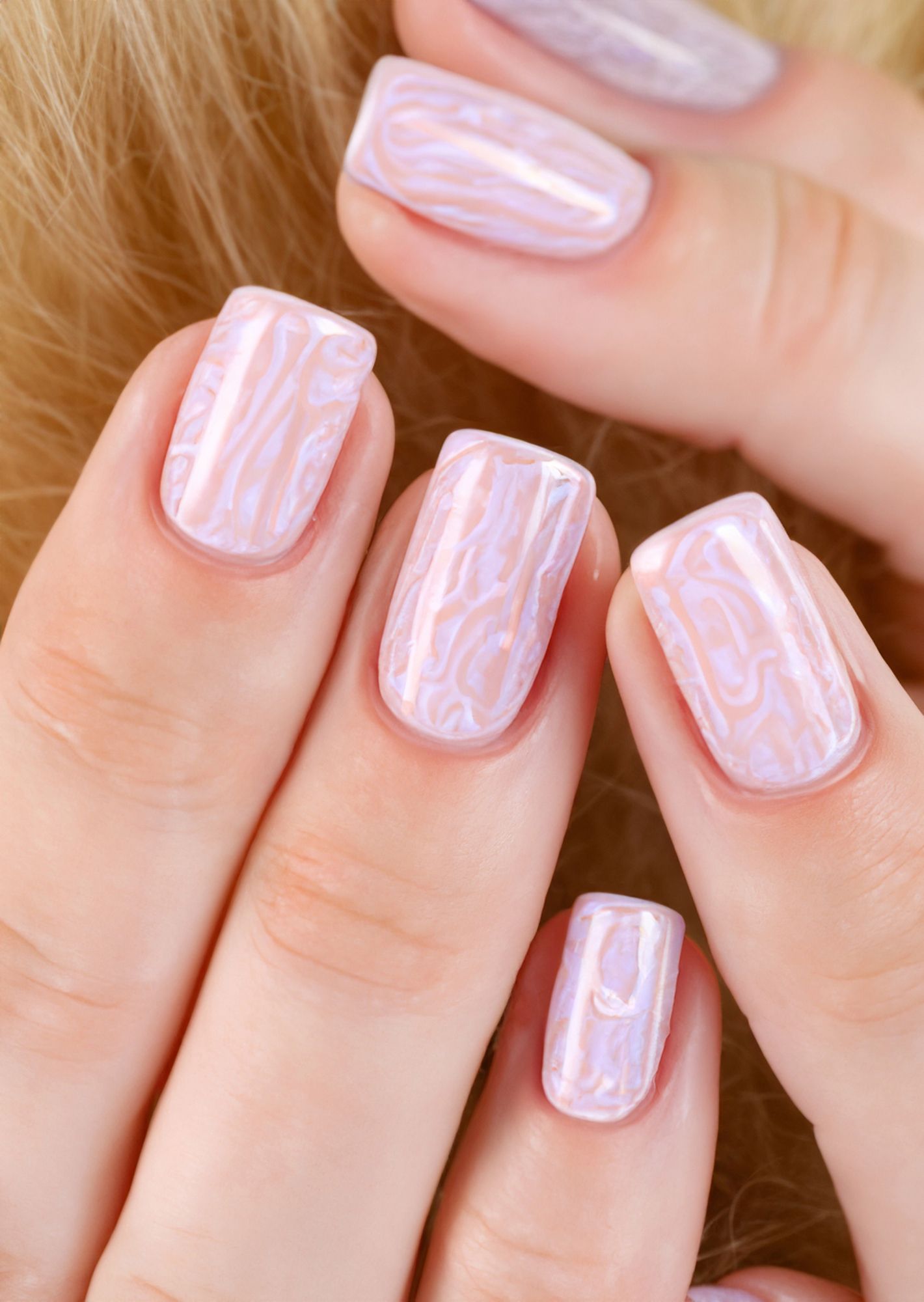 Primo piano di una mano con manicure marmorizzata rosa pallido e unghie quadrate lucide.