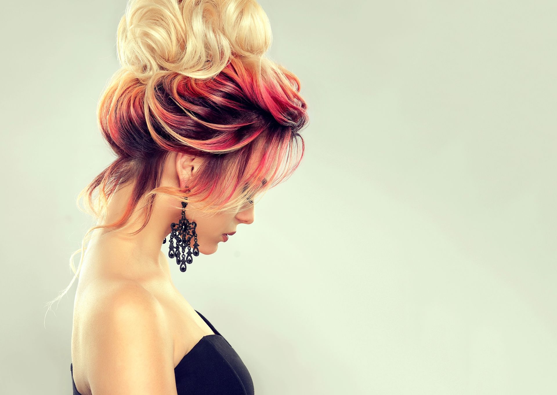 Profilo laterale di una donna con i capelli biondi e rosa raccolti, che indossa un top nero senza spalline e grandi orecchini pendenti.