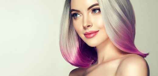 Ritratto di una donna bionda platino con le punte dei capelli rosa, sorridente su uno sfondo chiaro.