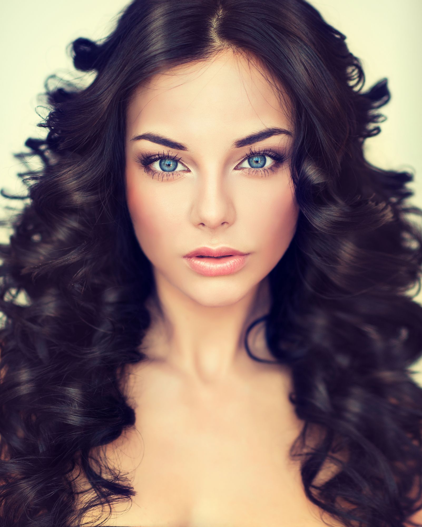 Ritratto di una donna con capelli scuri e ricci e occhi azzurri su sfondo chiaro.