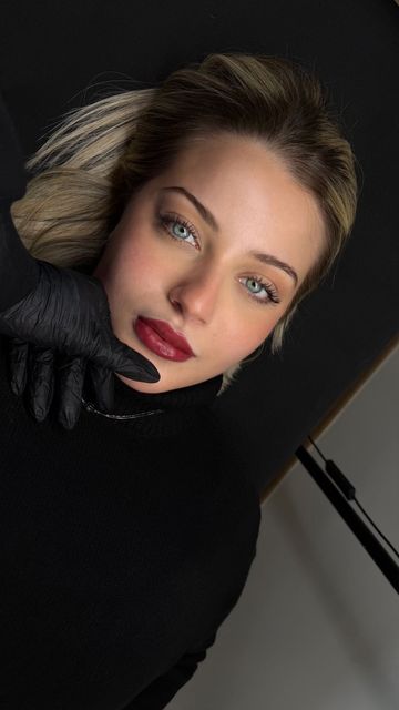 Ritratto di una donna con capelli scuri ed espressione neutra, che indossa un dolcevita grigio su sfondo chiaro.