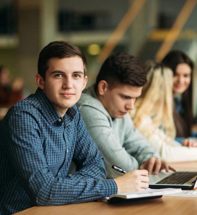 A group of young people are sitting at a table with laptops.