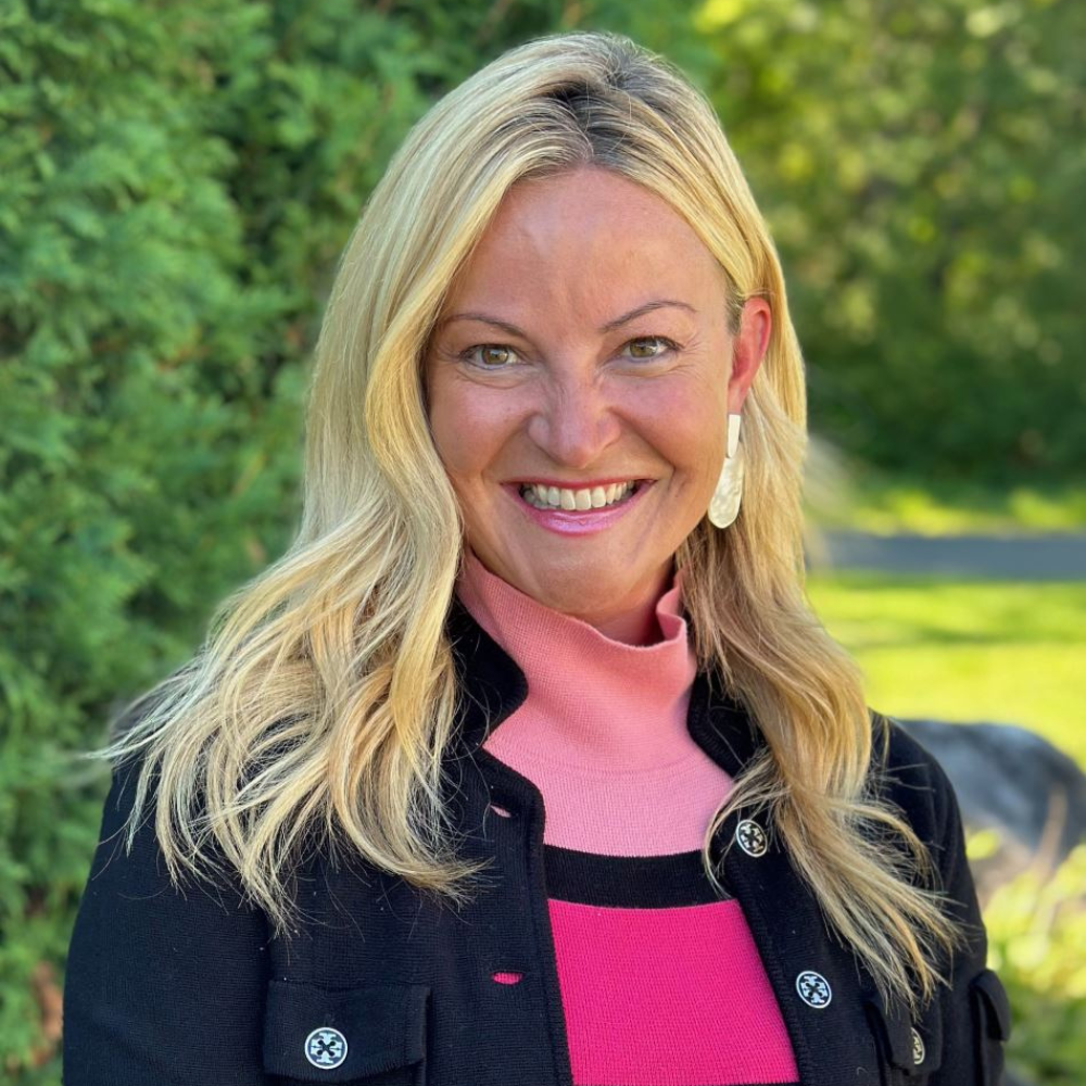 A woman wearing a pink sweater and a black jacket is smiling for the camera.