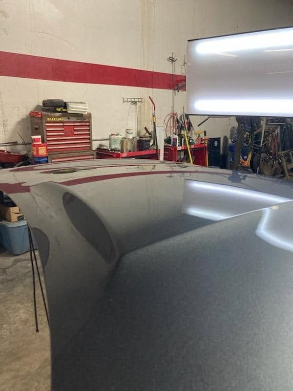 Gray car hood in auto shop with tools and equipment in the background