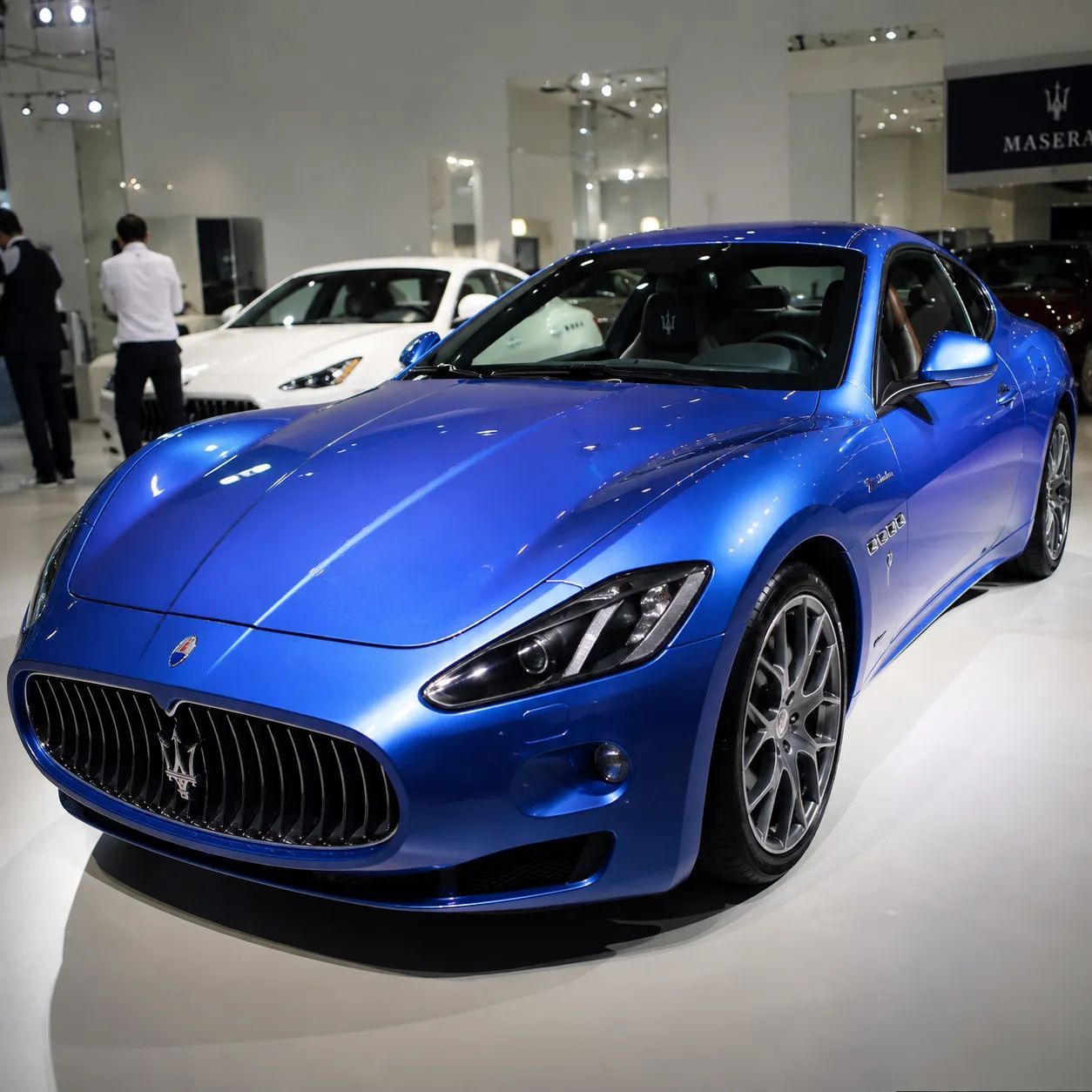 Blue sports car on display at an auto show, viewed from the front-left side.