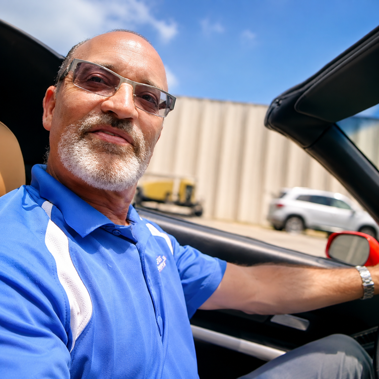 Smiling man in blue polo shirt driving a convertible on a sunny day