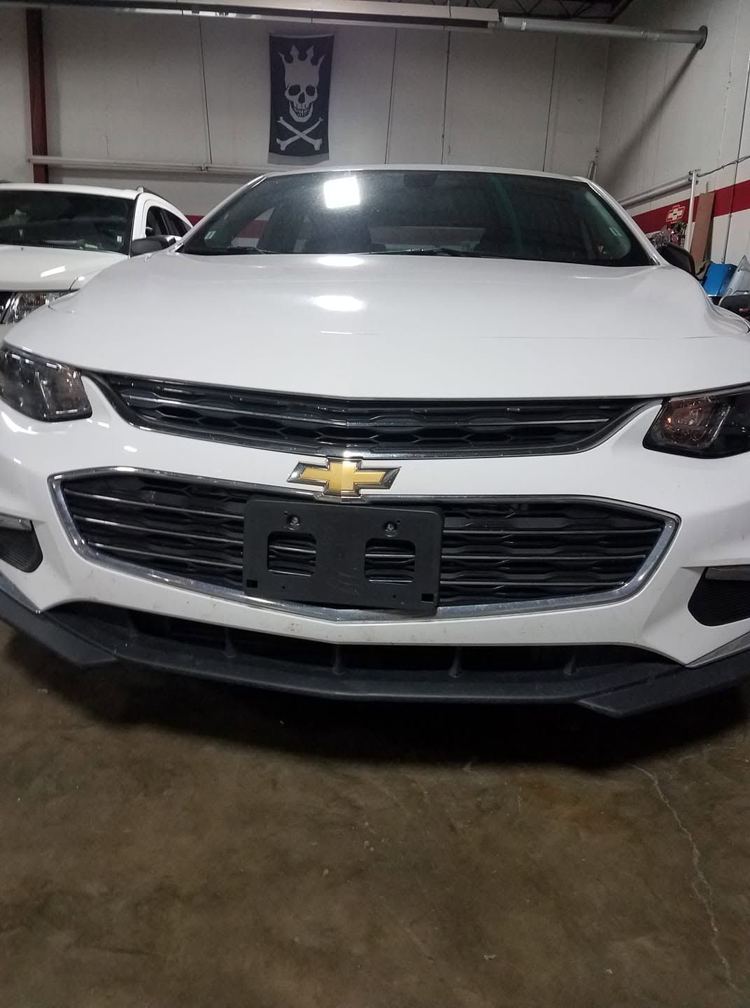 White Chevrolet sedan parked indoors in a garage, front view.