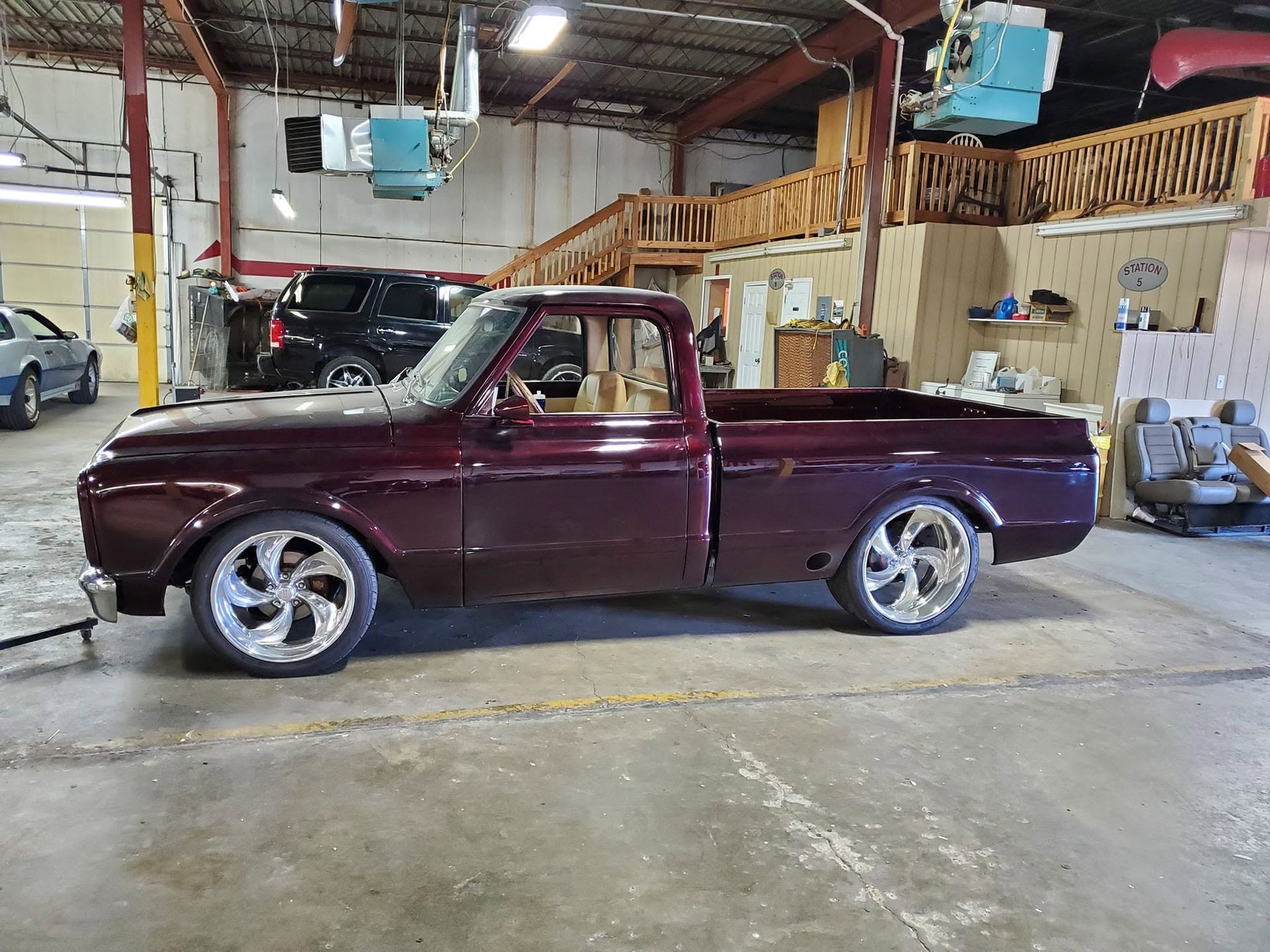 Maroon classic pickup truck in an auto shop garage, side view with chrome wheels.