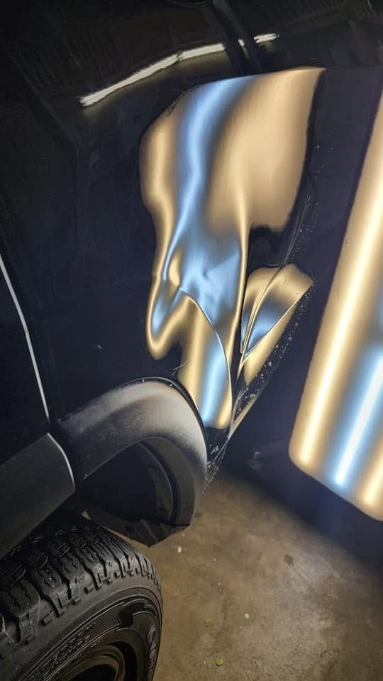 Damaged blue and gold car body panel with a wheel visible in a dim garage