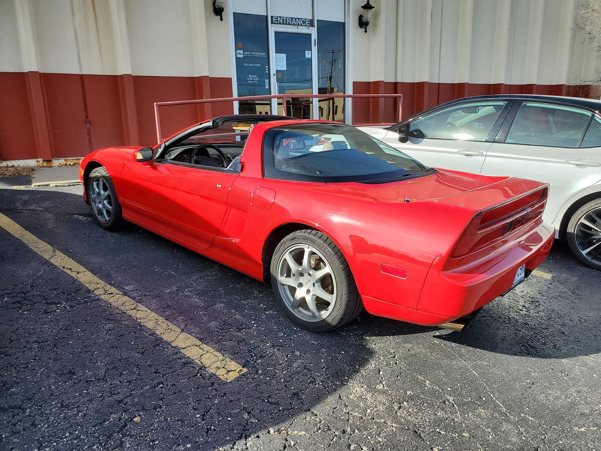 Red sports car parked beside a silver car outside a building