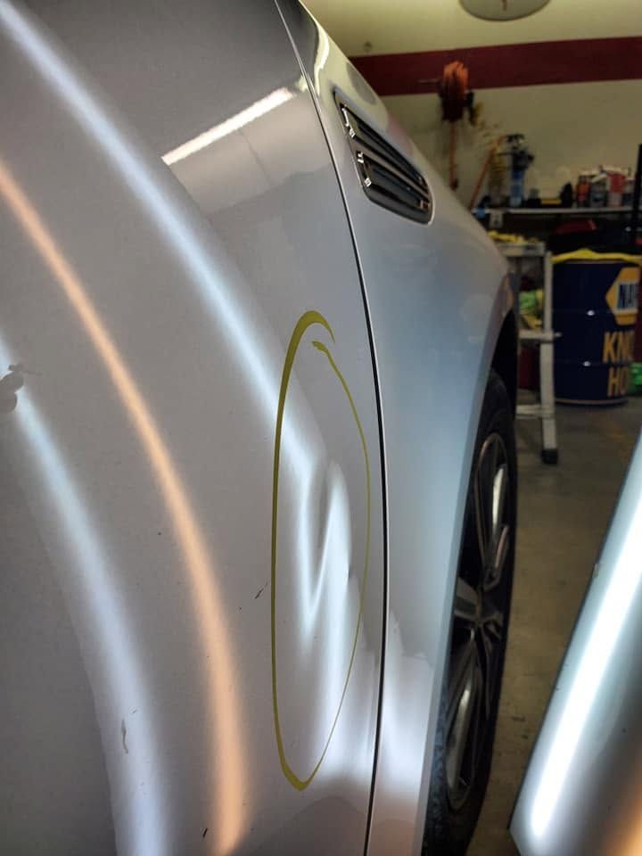 Silver car side panel with a dent circled in yellow in a garage