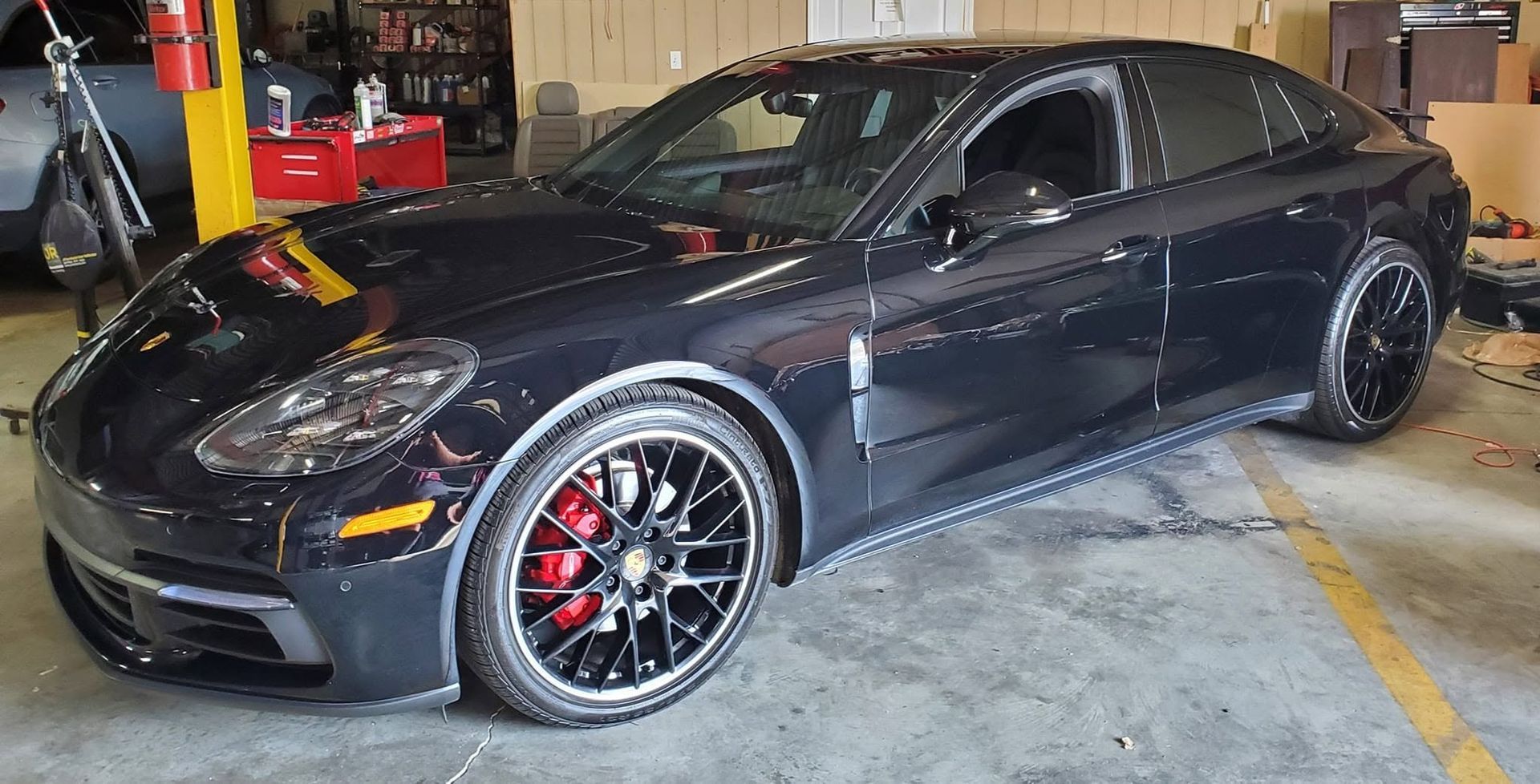 Black sports sedan in a garage, angled front-left, with red brake calipers and chrome wheels.