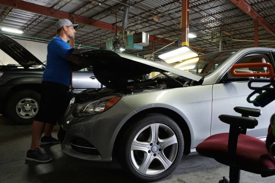 Person inspecting the engine of a silver car in a garage with the hood open