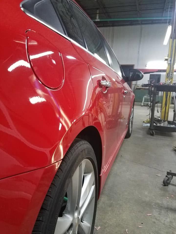 Red car in an auto shop, viewed from the side near a lift.