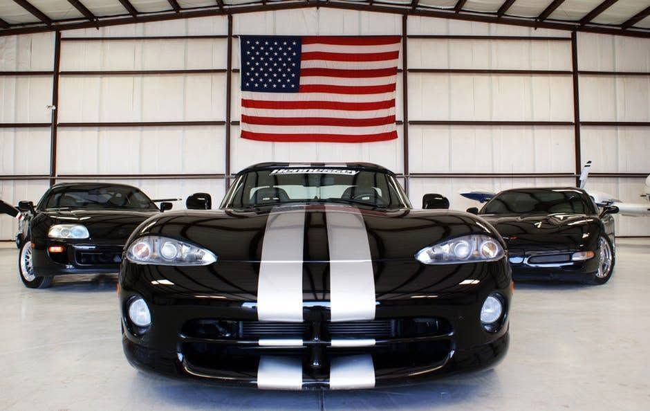 Three black sports cars in a garage, with an American flag hanging behind the center car.