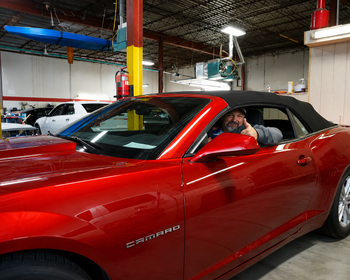 Man sitting in a red convertible sports car inside an indoor garage