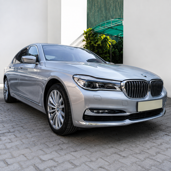 Silver BMW sedan parked on a paved driveway beside a white wall and greenery