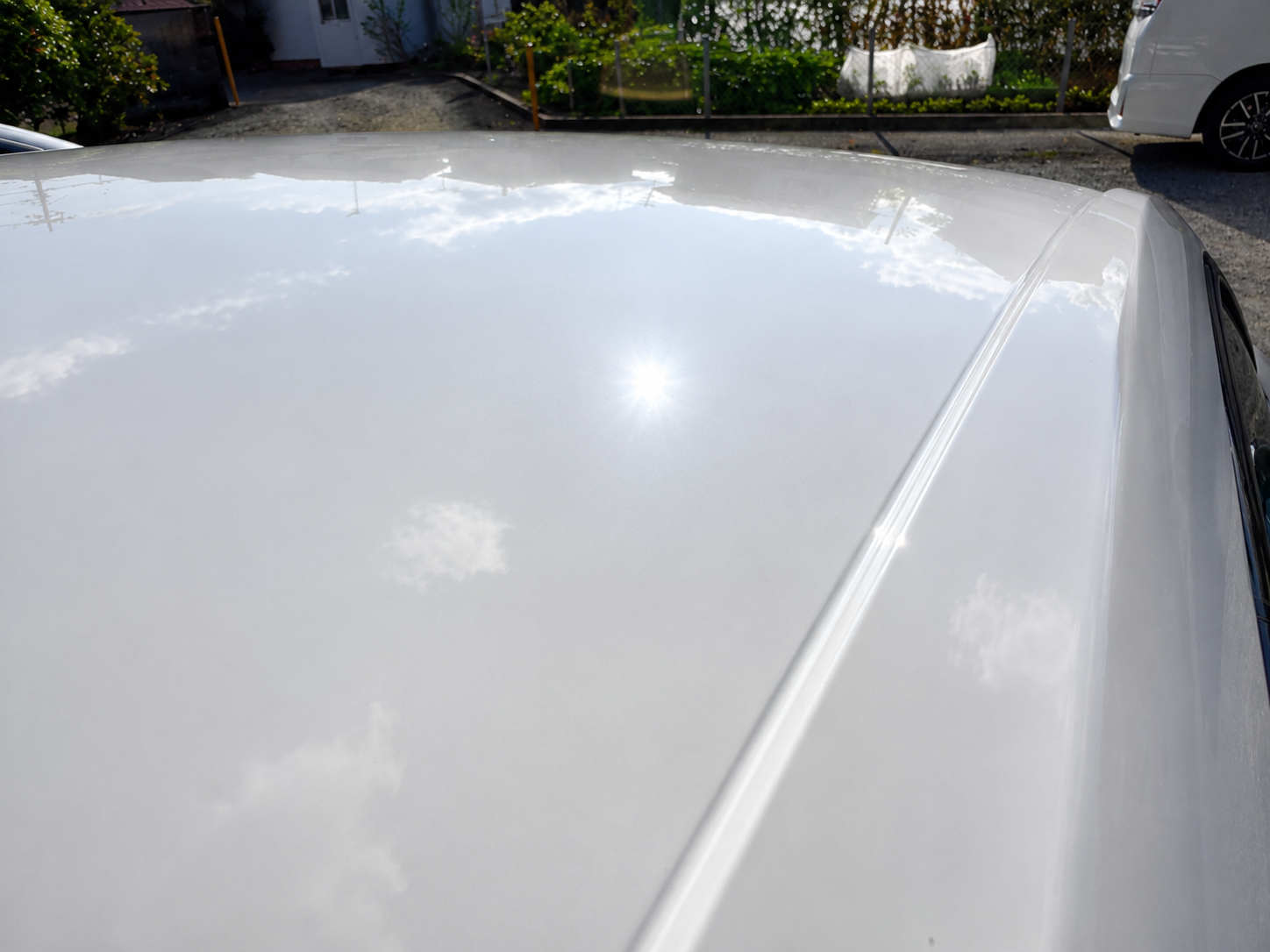 Close-up of a white car roof reflecting the sky and clouds outdoors