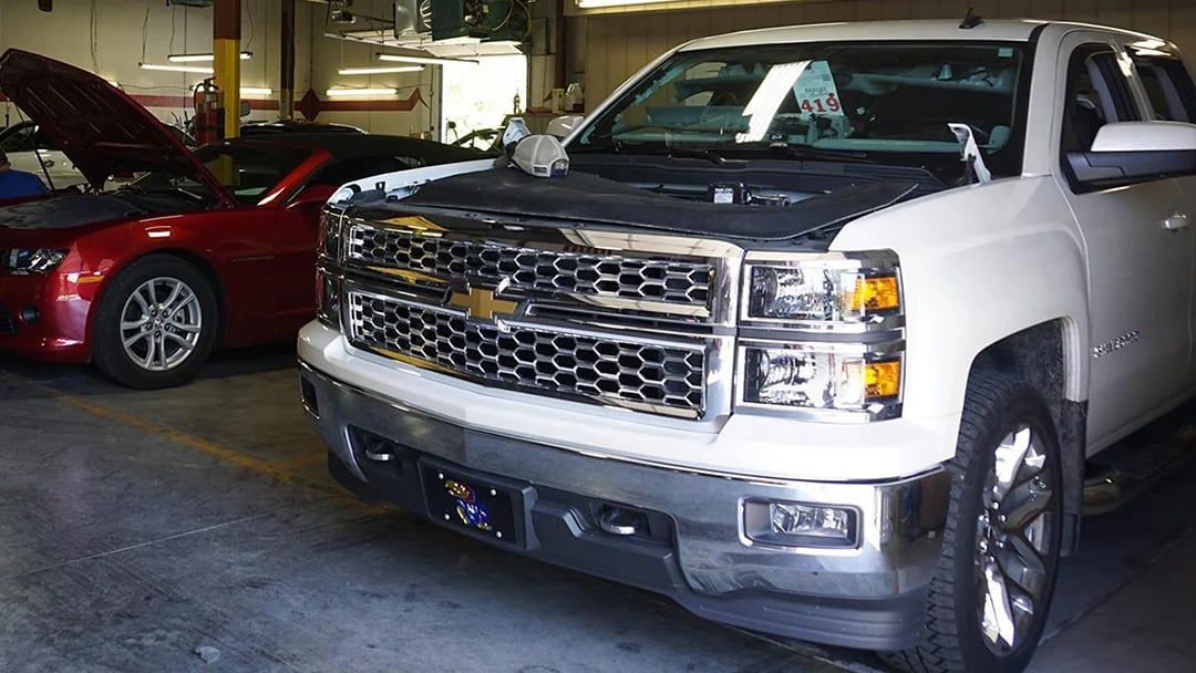 Silver Chevrolet pickup parked indoors beside a red car in a garage