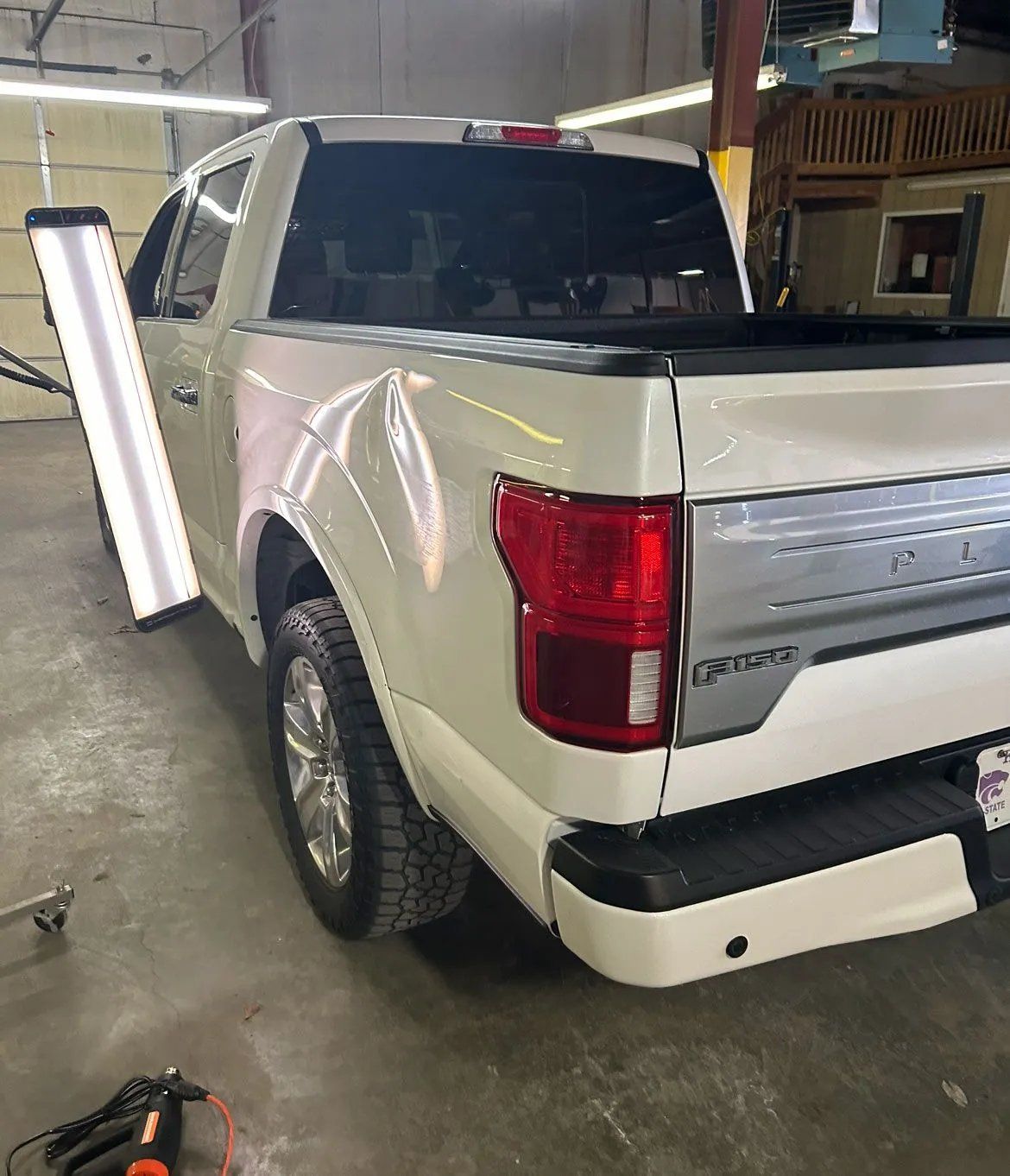 White pickup truck parked indoors in a garage, rear three-quarter view with open door.