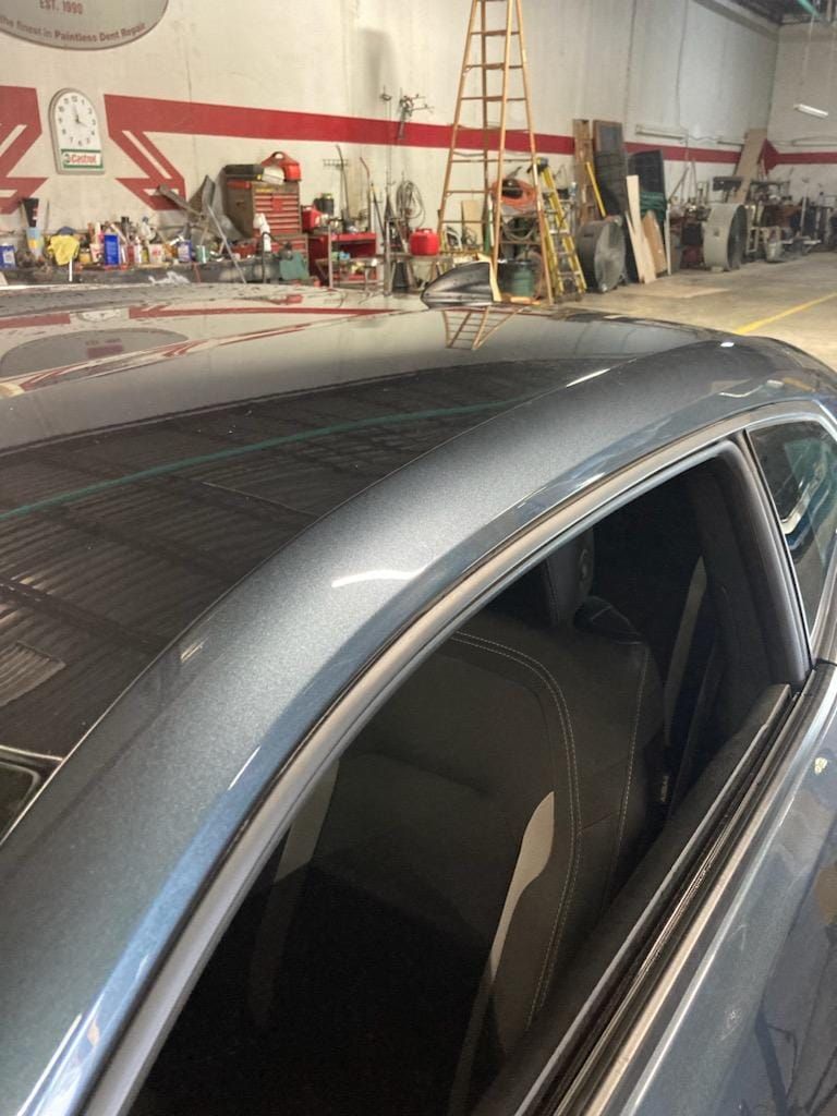 Gray car in a workshop with an open window and roof rack, tools and ladders in the background
